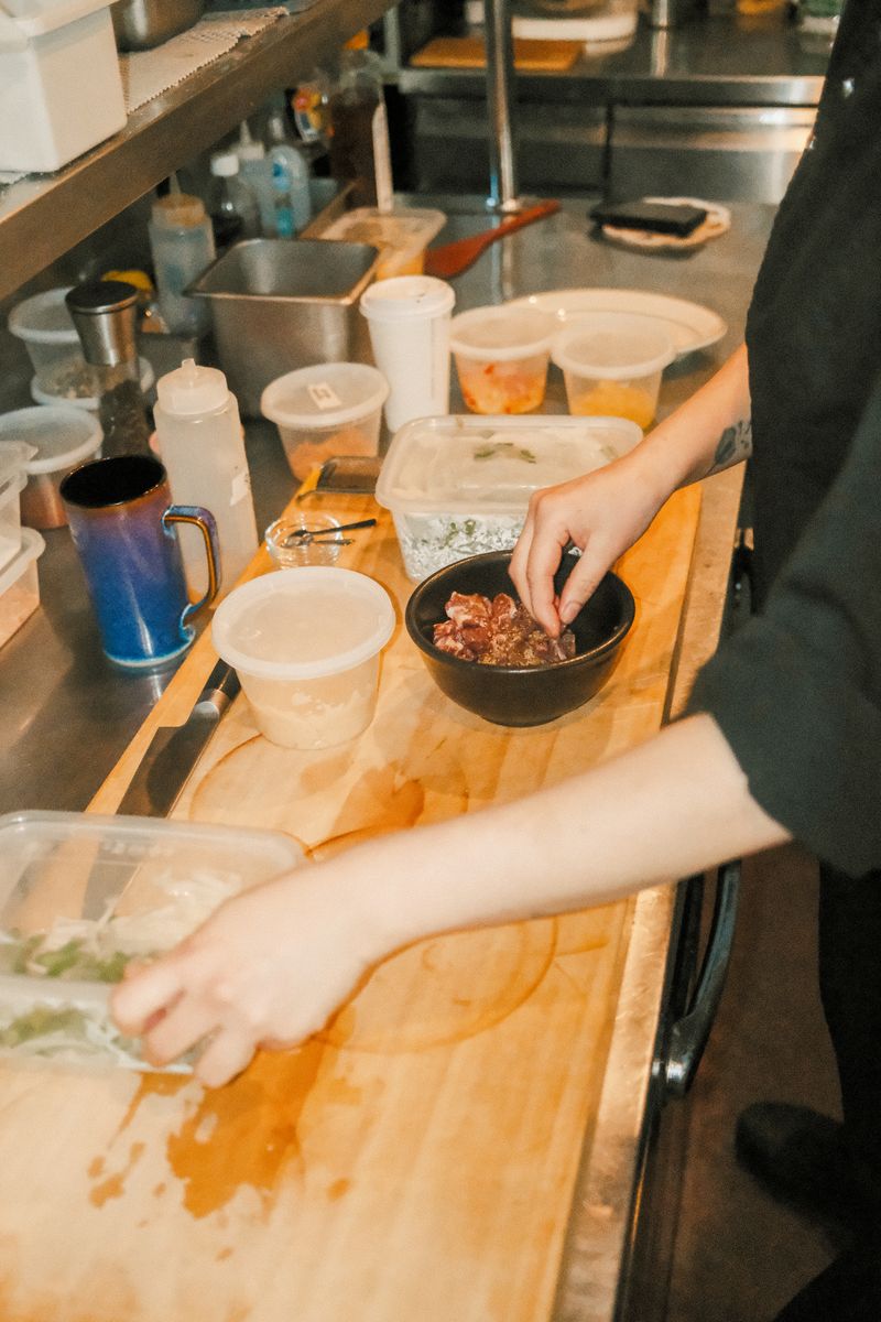 A parent and child reviewing a handwritten grocery list together at a kitchen table with reusable shopping bags nearby.